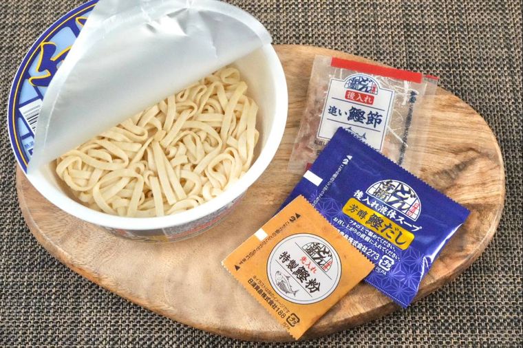 木のカッティングボードにのったカップうどんと別添えの調味料