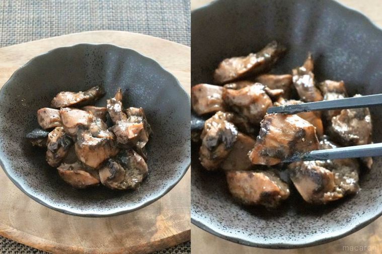 木のカッティングボードにのった黒い器に盛られた砂肝の炭火焼きを黒い箸で持ち上げる様子