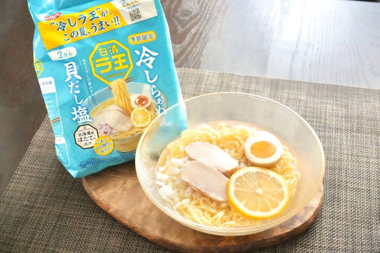 木のカッティングボードにのったガラスの器に盛られた冷やしラーメンと水色のパッケージ