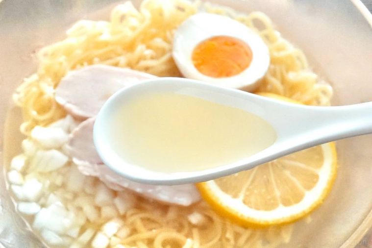 ガラスの器に盛られた冷やしラーメンのスープを白いれんげですくう様子