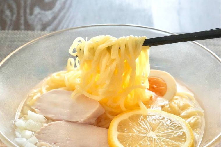 ガラスの器に盛られた冷やしラーメンの麺を黒い箸で持ち上げる様子