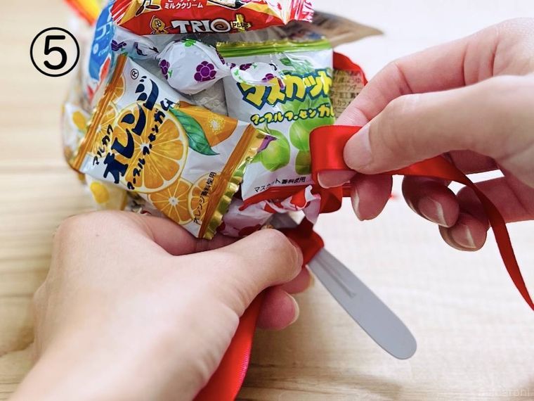 キャンディ風にラッピングしたギフトの持ち手にリボンを結んでいる様子