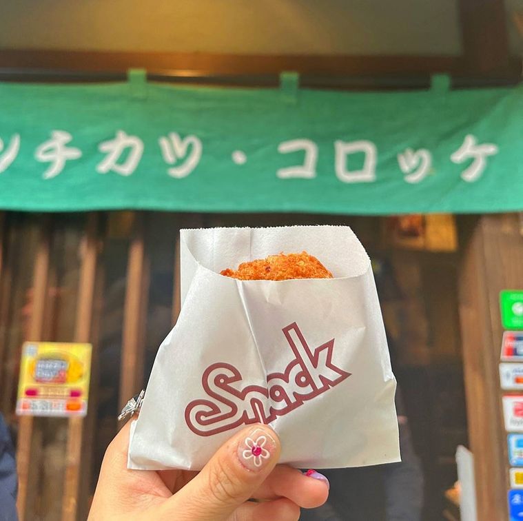 緑の暖簾がかかった店頭と白い袋に入ったコロッケ