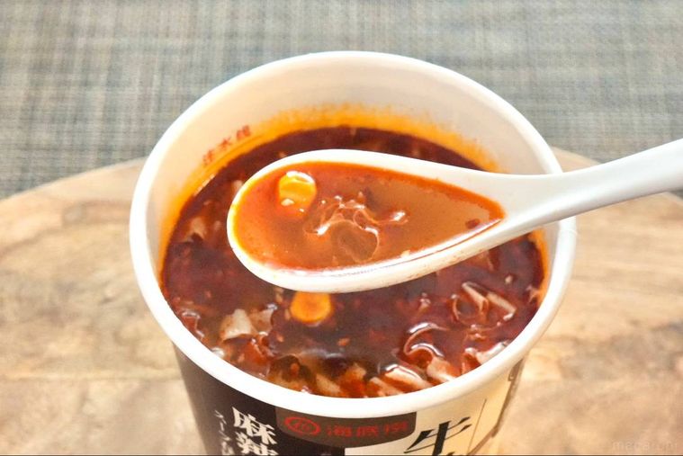 木のカッティングボードにのったカップ麻辣湯を白いれんげで食べる様子