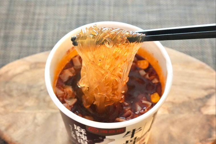 木のカッティングボードにのったカップ麻辣湯の春雨を黒い箸で食べる様子