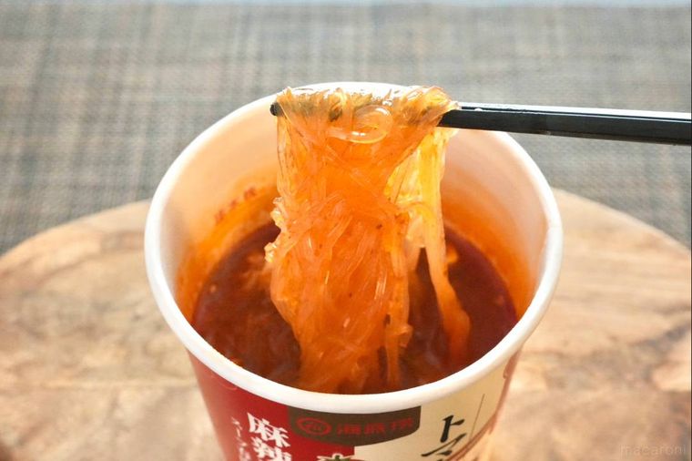 木のカッティングボードにのったカップ麻辣湯の春雨を黒い箸で食べる様子