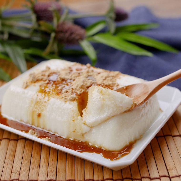 黒蜜ときなこがかかった豆腐プリンを、木のスプーンですくっている様子