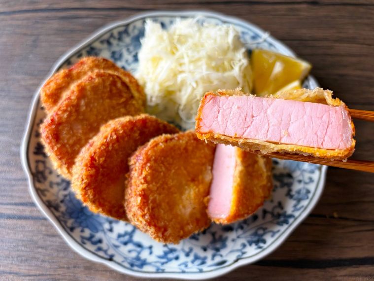 和皿に盛られた分厚いハムカツを箸上げした様子