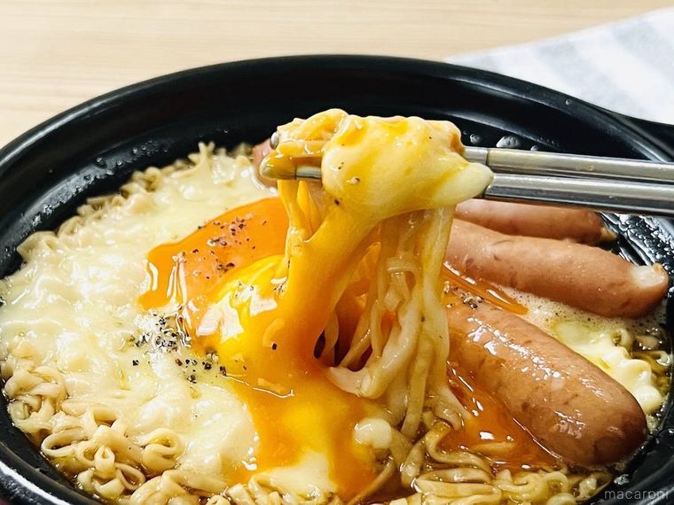 ウインナー、チーズ、卵黄がのったチキンラーメンの麺をすくっている様子