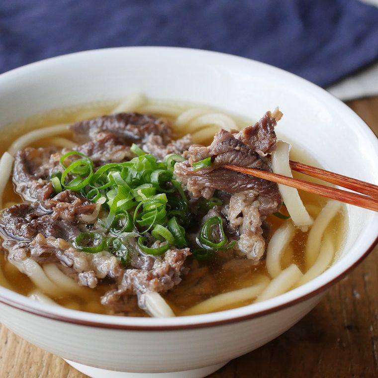 白い丼茶碗に盛られた肉うどんを箸でつまんでいる