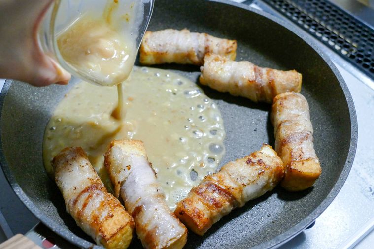 フライパンに並ぶ厚揚げの豚バラ巻きに合わせ調味料を加える様子
