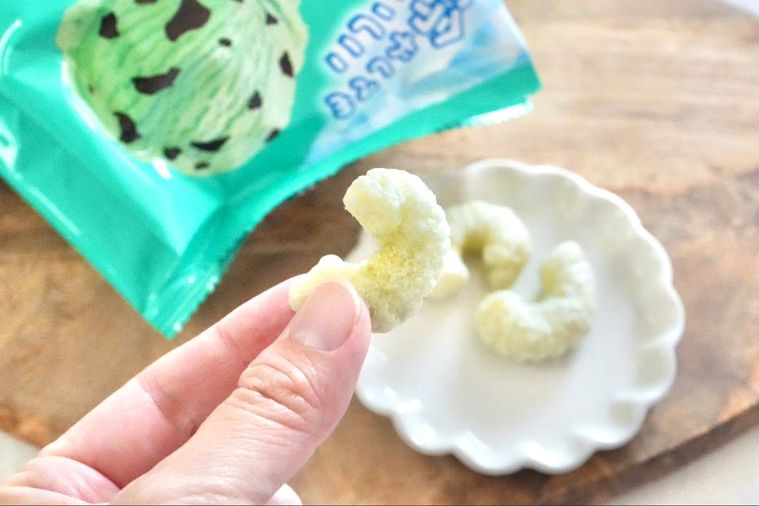 木のカッティングボードと白い小皿にのったチョコミント味のキャラメルコーンを手に持つ様子