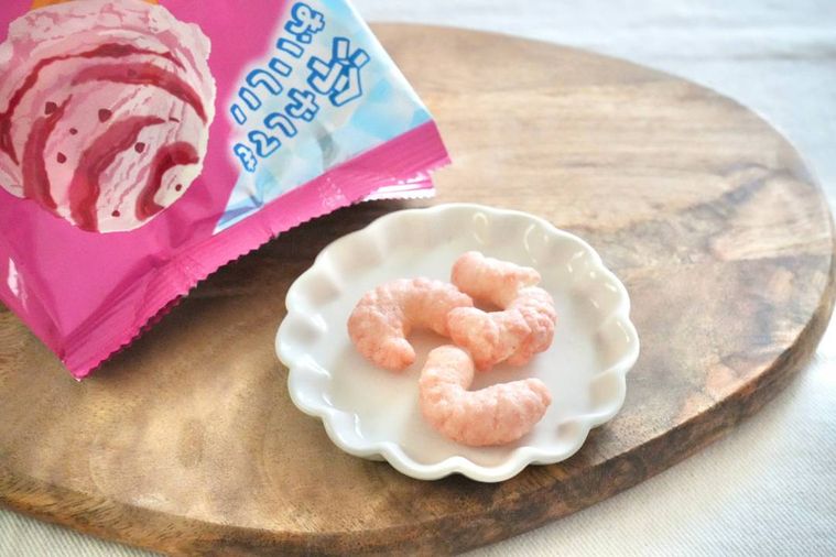 木のカッティングボードと白い小皿にのったストロベリーアイス味のキャラメルコーンとピンク色のパッケージ