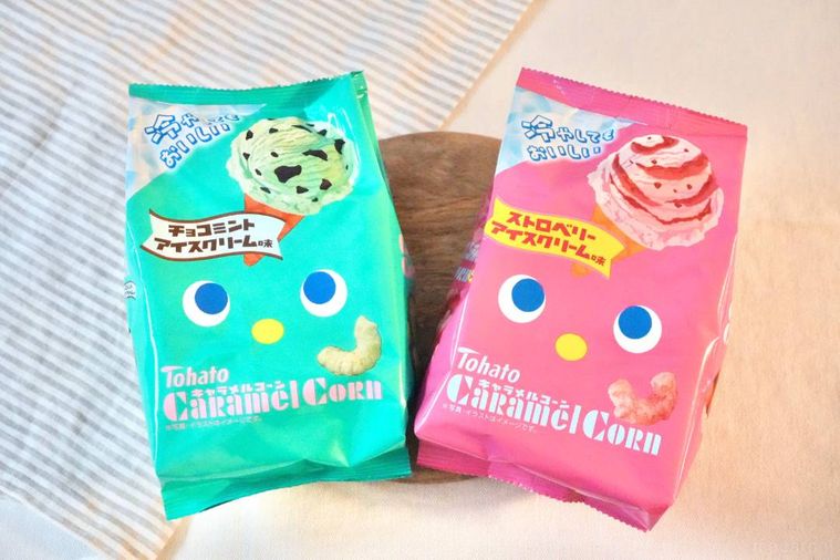 木のカッティングボードにのったアイスクリーム味のキャラメルコーンのミント色とピンク色のパッケージ