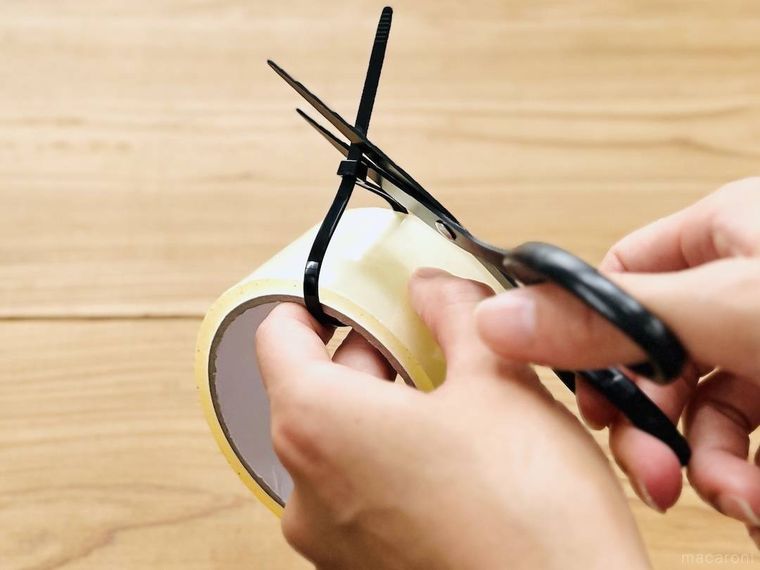 透明テープに取り付けた結束バンドをハサミで切っている様子
