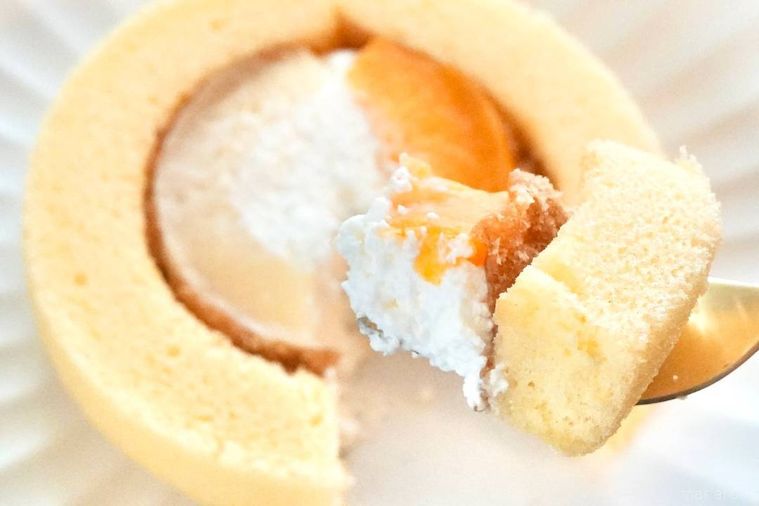 白い皿にのった黄桃と白桃のプレミアムロールケーキを金色のフォークで食べる様子