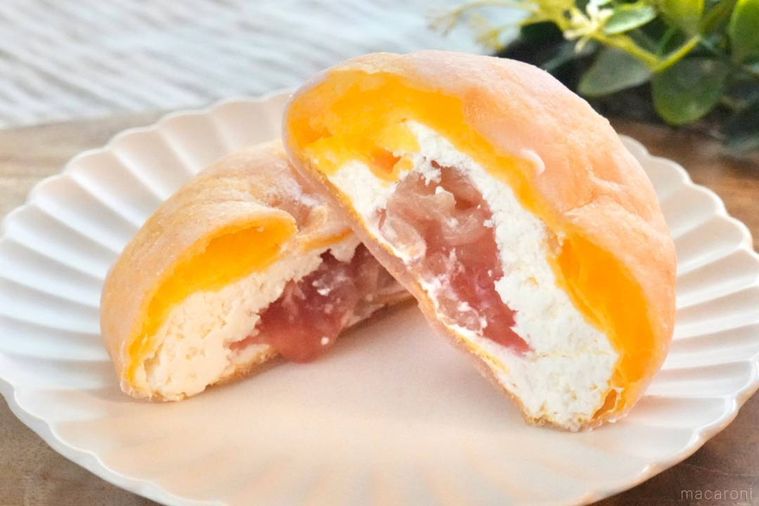 木のカッティングボードと白い皿にのった桃のシュークリームの断面から桃のダイス果肉がこぼれる様子