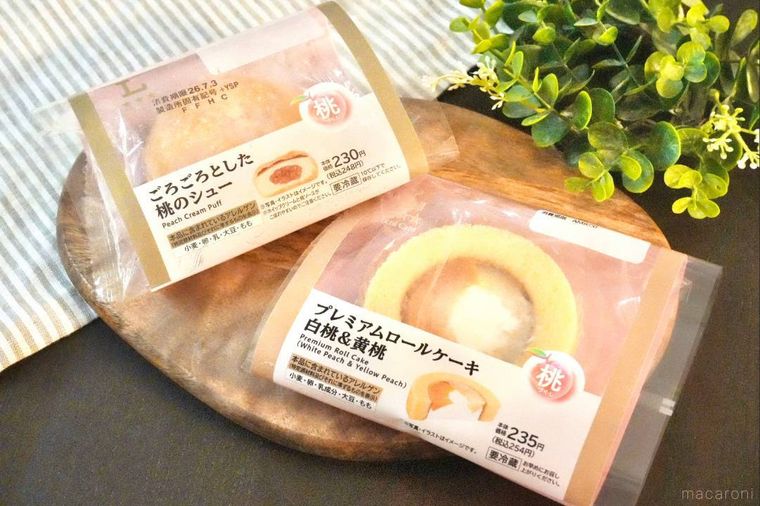 木のカッティングボードにのった桃のシュークリームとプレミアムロールケーキのピンク色のパッケージ