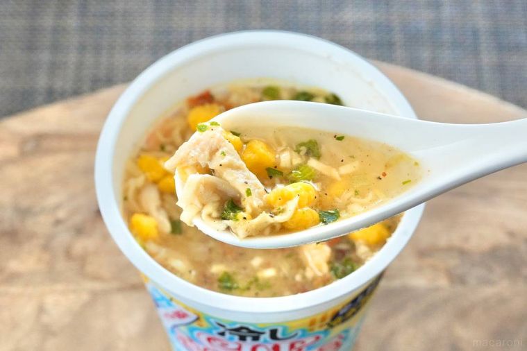木のカッティングボードにのった冷しカップヌードル鶏塩レモン味のスープを白いれんげですくう様子