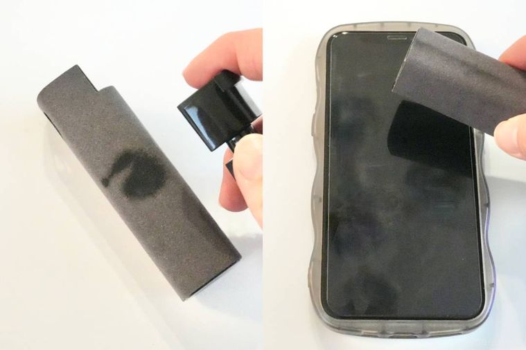 スクリーンクリーナーのクロスにスプレーを吹きかけてスマートフォンの画面を拭く様子