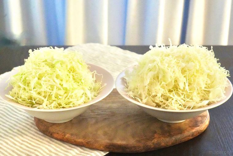 木のカッティングボードにのった器に盛られた千切りキャベツ