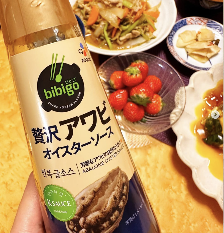 テーブルの上に料理が並んでいて、手にコストコの贅沢アワビオイスターソースを持っている