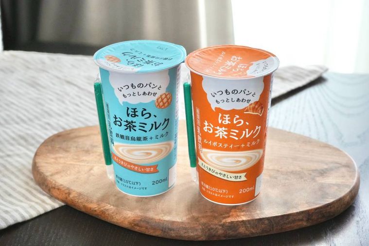 木のカッティングボードにのった水色とオレンジ色のパッケージカップのティー飲料とストライプの布
