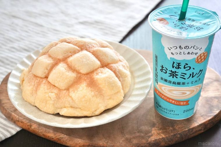 木のカッティングボードにのった水色のパッケージの鉄観音烏龍茶ミルクと白い器にのったメロンパンとストライプの布