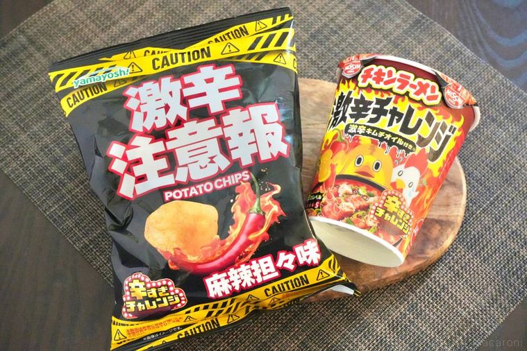 木のカッティングボードにのった激辛チップスとカップのチキンラーメン