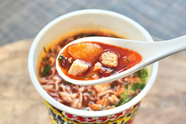 木のカッティングボードにのったカップの激辛チキンラーメンのスープを白いれんげですくう様子