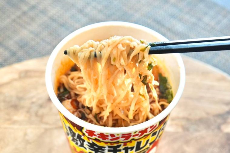 木のカッティングボードにのった激辛チキンラーメンの麺を黒い箸で持ち上げる様子