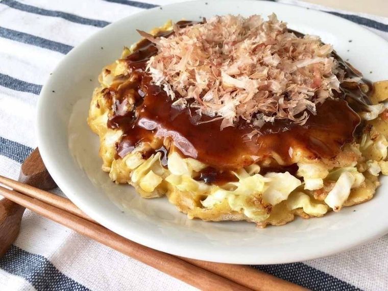 グレーの皿に盛られたかつおぶしやソースがのったお好み焼き