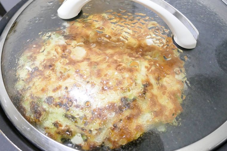 お好み焼きをフライパンで蒸し焼きにしている様子