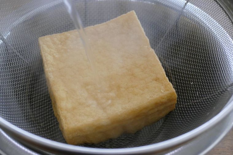 ザルにのせた厚揚げに熱湯をまわしかける様子