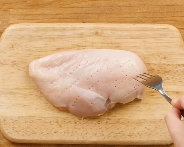まな板に置いた鶏胸肉にフォークを刺しているところ