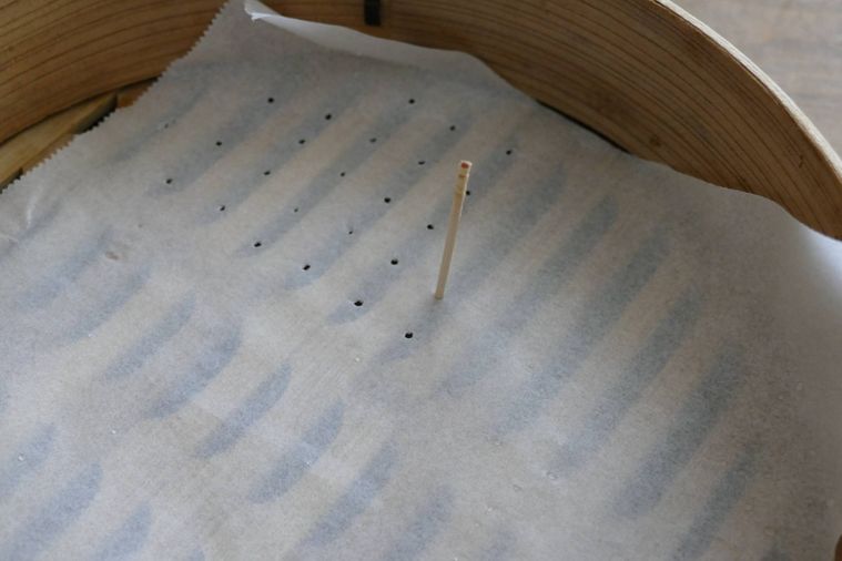 せいろに敷いたクッキングシートにつまようじで穴を開ける様子