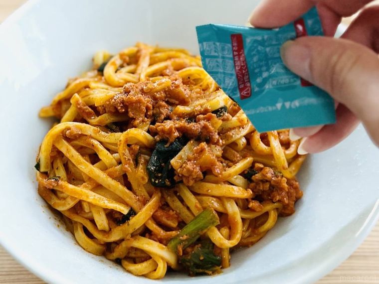 もちっと麺と濃厚だれの汁なし担々麺に唐辛子をかけている様子