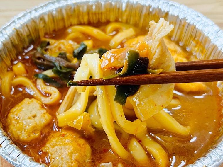 炒め唐辛子が効いた旨辛チゲうどんのうどんを箸ですくった様子