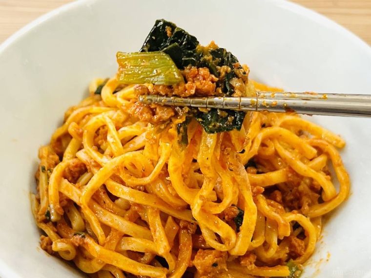 もちっと麺と濃厚だれの汁なし担々麺の麺と具材を箸で持ち上げている様子