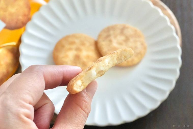 木のカッティングボードと白い皿にのったファミマ味のソフトせんべいを手に持ち食べる様子