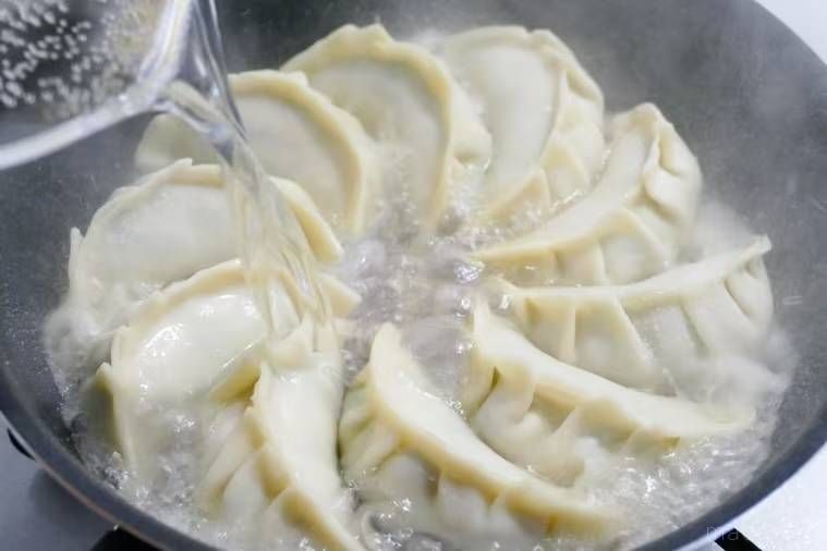 餃子を並べたフライパンに熱湯を注いでいる様子