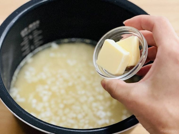 米、水、コンソメ、玉ねぎが入った炊飯釜にバターを入れようとしている様子