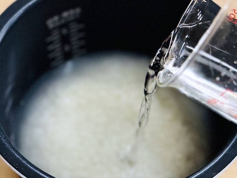 米が入った炊飯釜に水を注いでいる様子