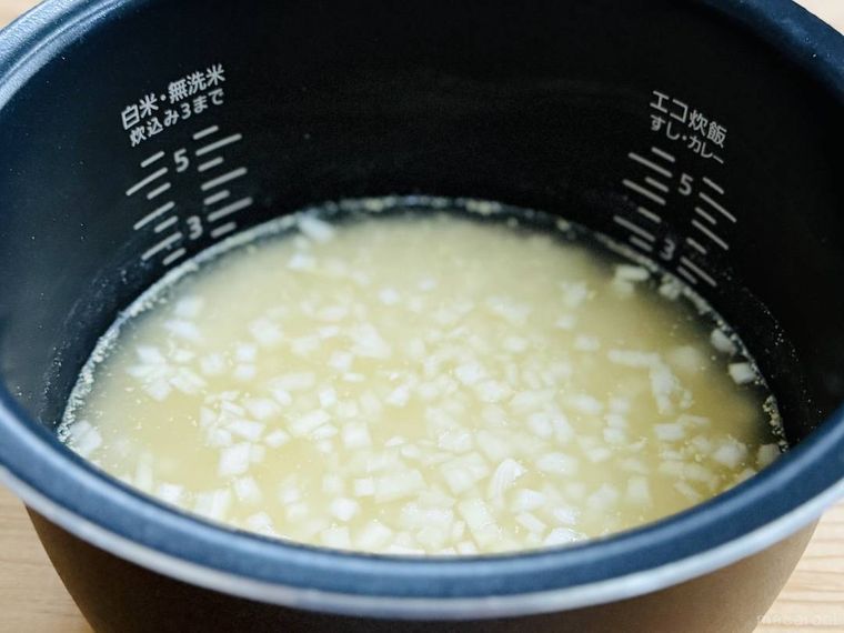 米、水、コンソメが入った炊飯釜に玉ねぎを散らした様子