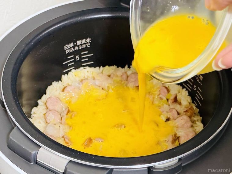 チャーハンが入った炊飯釜に溶き卵を回し入れている様子