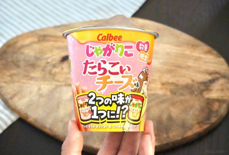 木のカッティングボードと黄色とピンク色のパッケージのじゃがりこたらこチーズ味を手に持つ様子