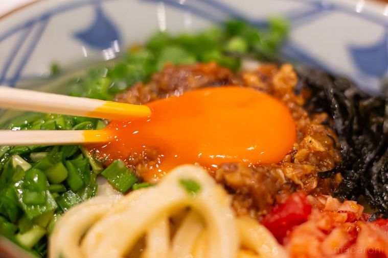 丸亀製麺ガツンとニンニク肉辛まぜうどんひと口ごはん、トマト酢つきの卵黄を割っている