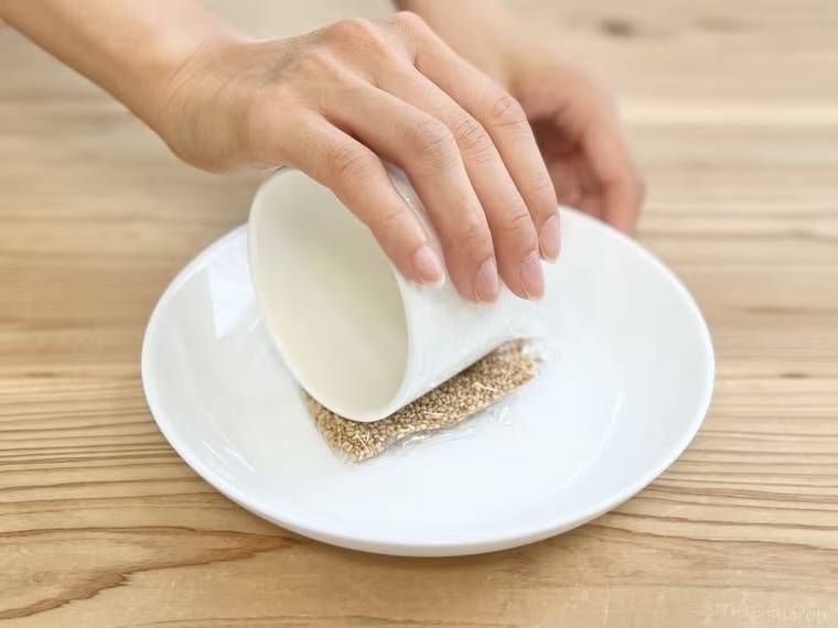 いりごまをラップで包み、筒状の器ですりつぶしている様子