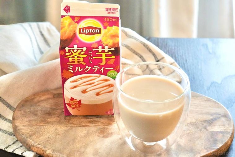 木のカッティングボードにのった蜜芋ミルクティー入りのグラスとさつまいも色の紙パックパッケージ