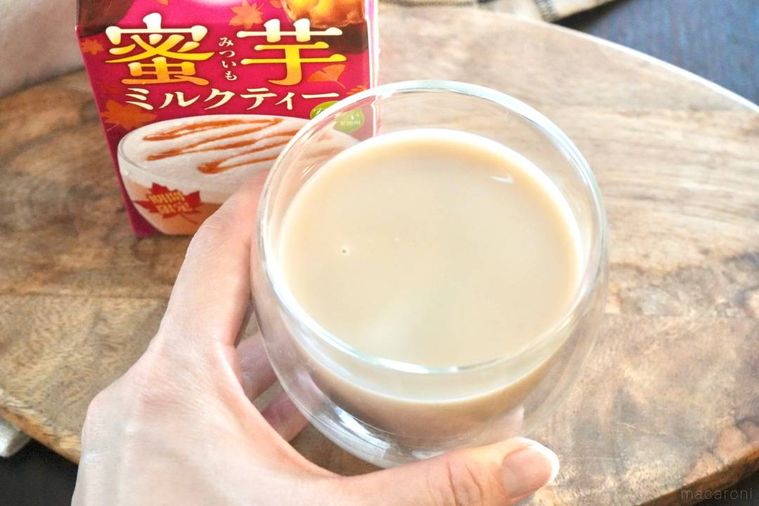 木のカッティングボードにのった蜜芋ミルクティー入りのグラスを手に持つ様子